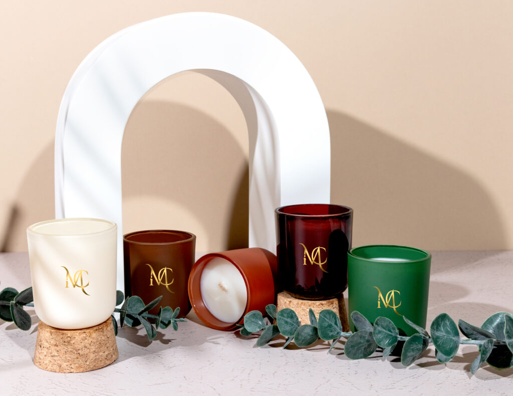 Styled lifestyle product photography of candle collection with warm neutral backdrop and greenery.